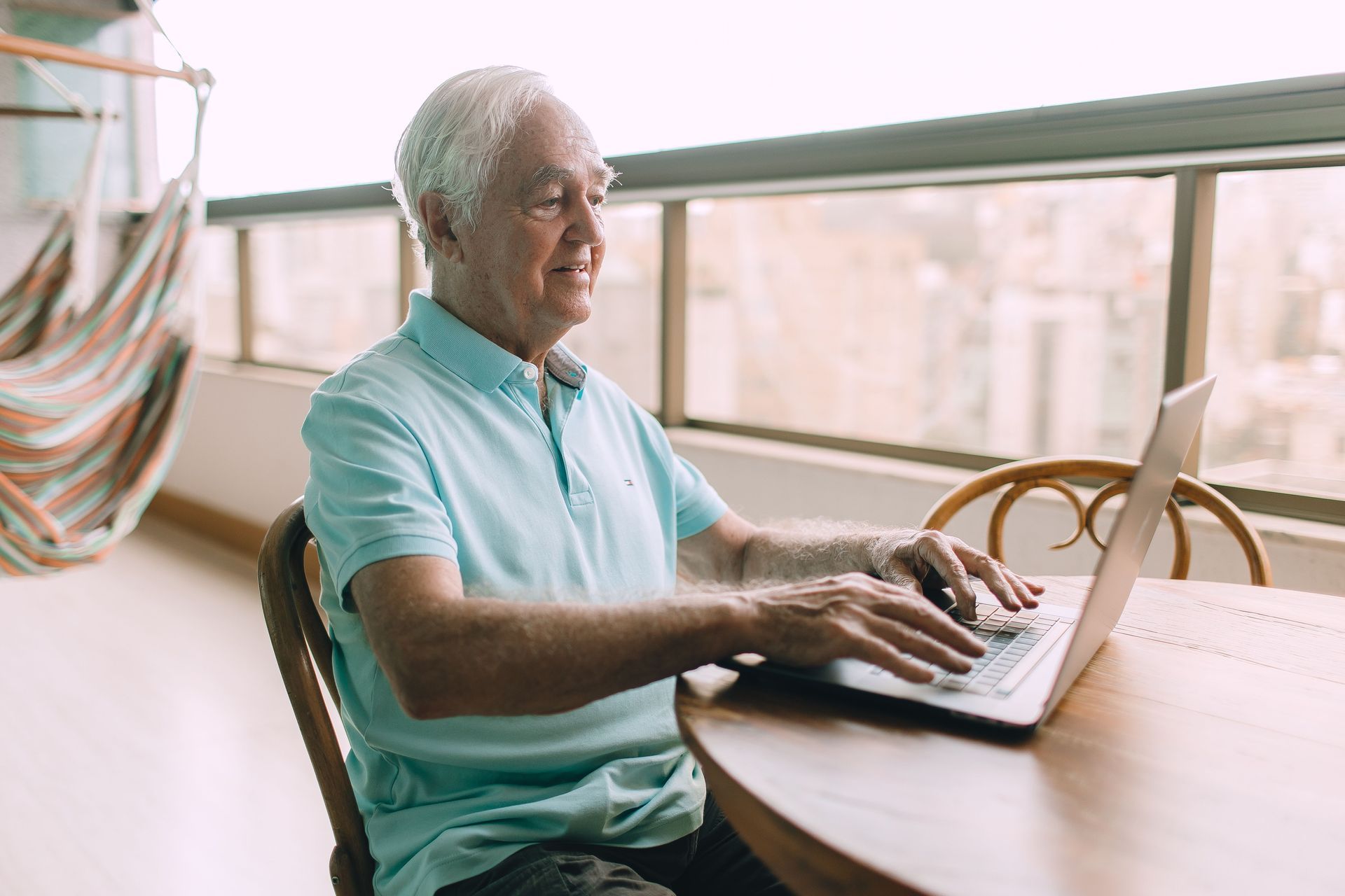 Older man using a laptop at a sunlit table by a window