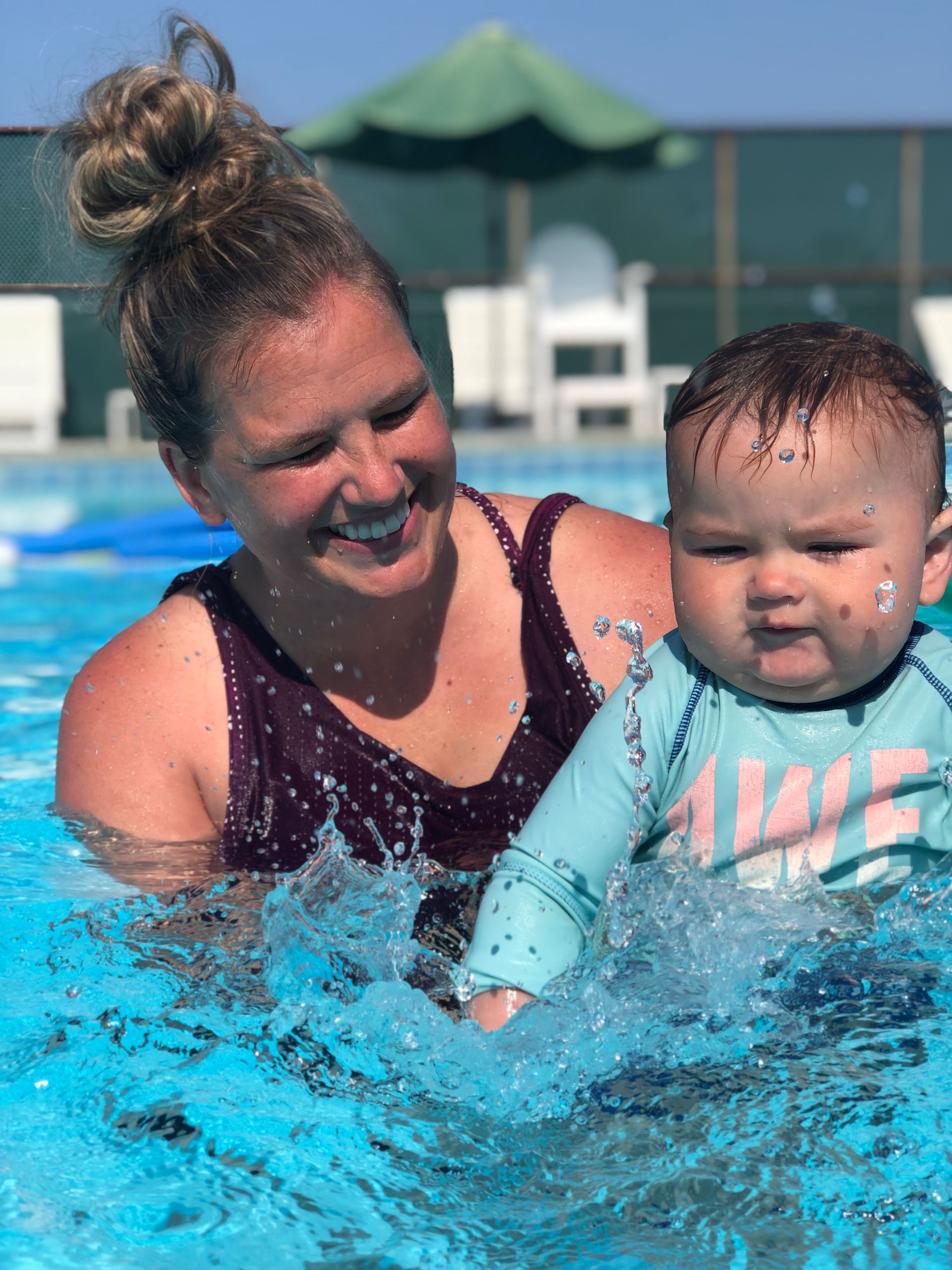 Woman and baby splashing in a swimming pool, smiling in bright sunlight