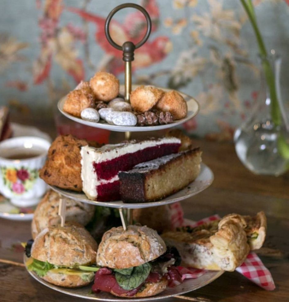 Drielaags serveerschaal met gebak: sandwiches, taartpunten, scones en andere zoetigheden.
