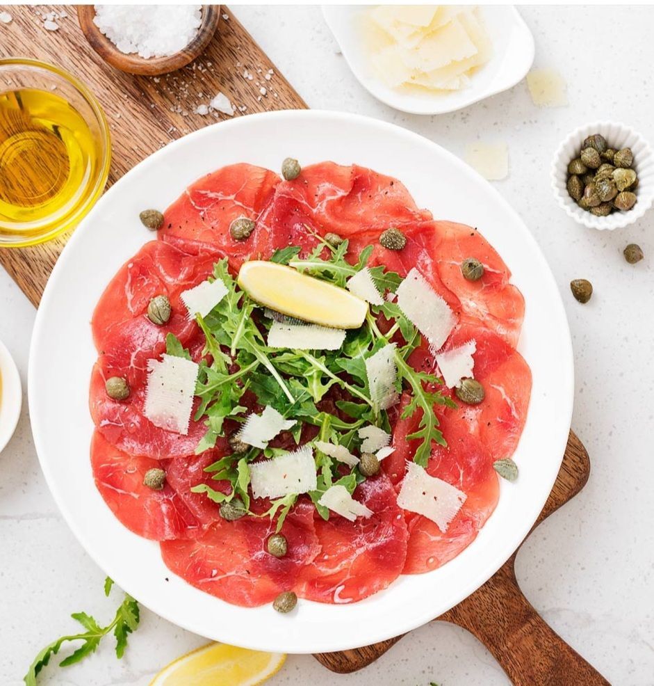 Carpaccio: dun gesneden rood vlees, rucola, Parmezaanse kaas, kappertjes, citroen en olijfolie.
