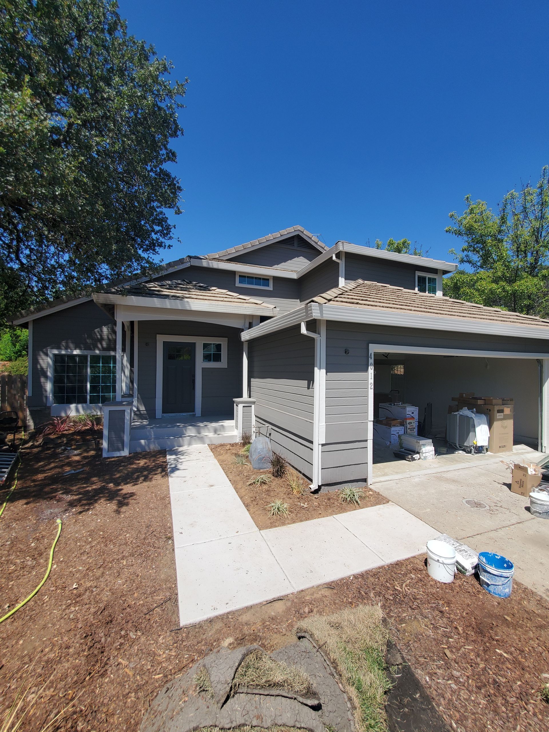 Gray house with walkway, driveway, and landscaping on a sunny day.