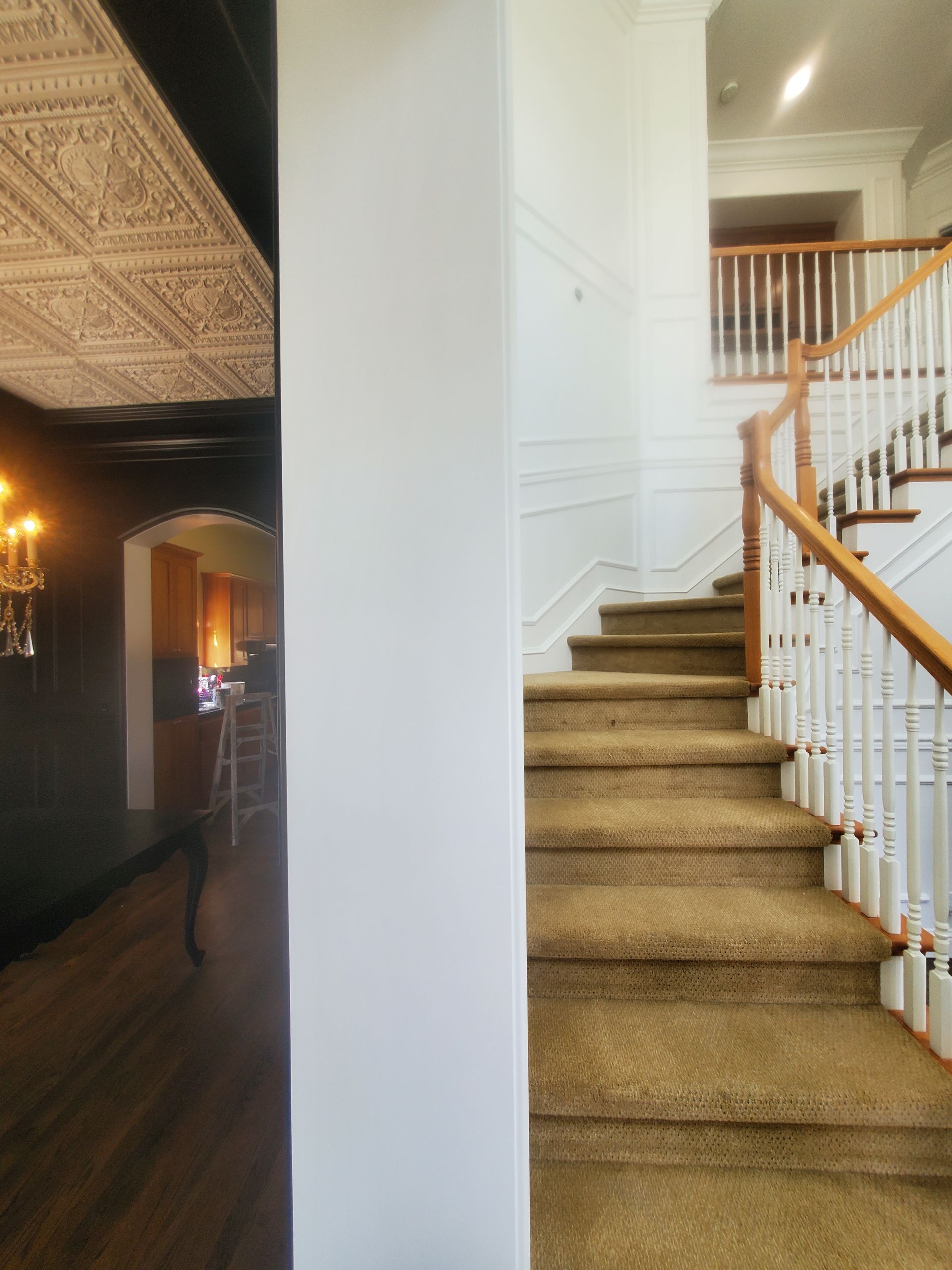 Hallway with stairs and column; wood floor to the left, carpeted stairs to the right, white walls, and a decorative ceiling.