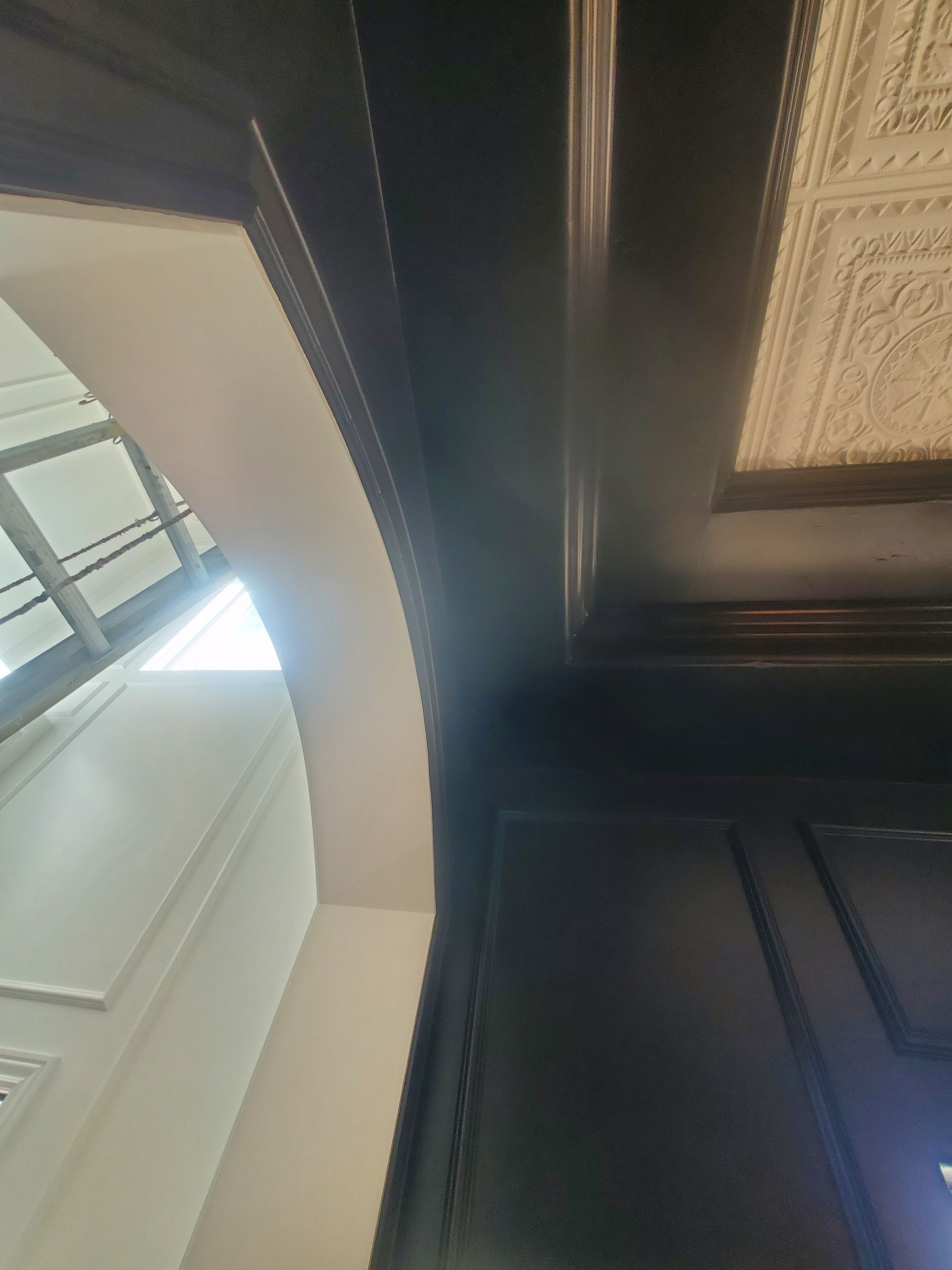 Dark wood trim frames a white arched doorway and an ornate ceiling panel.