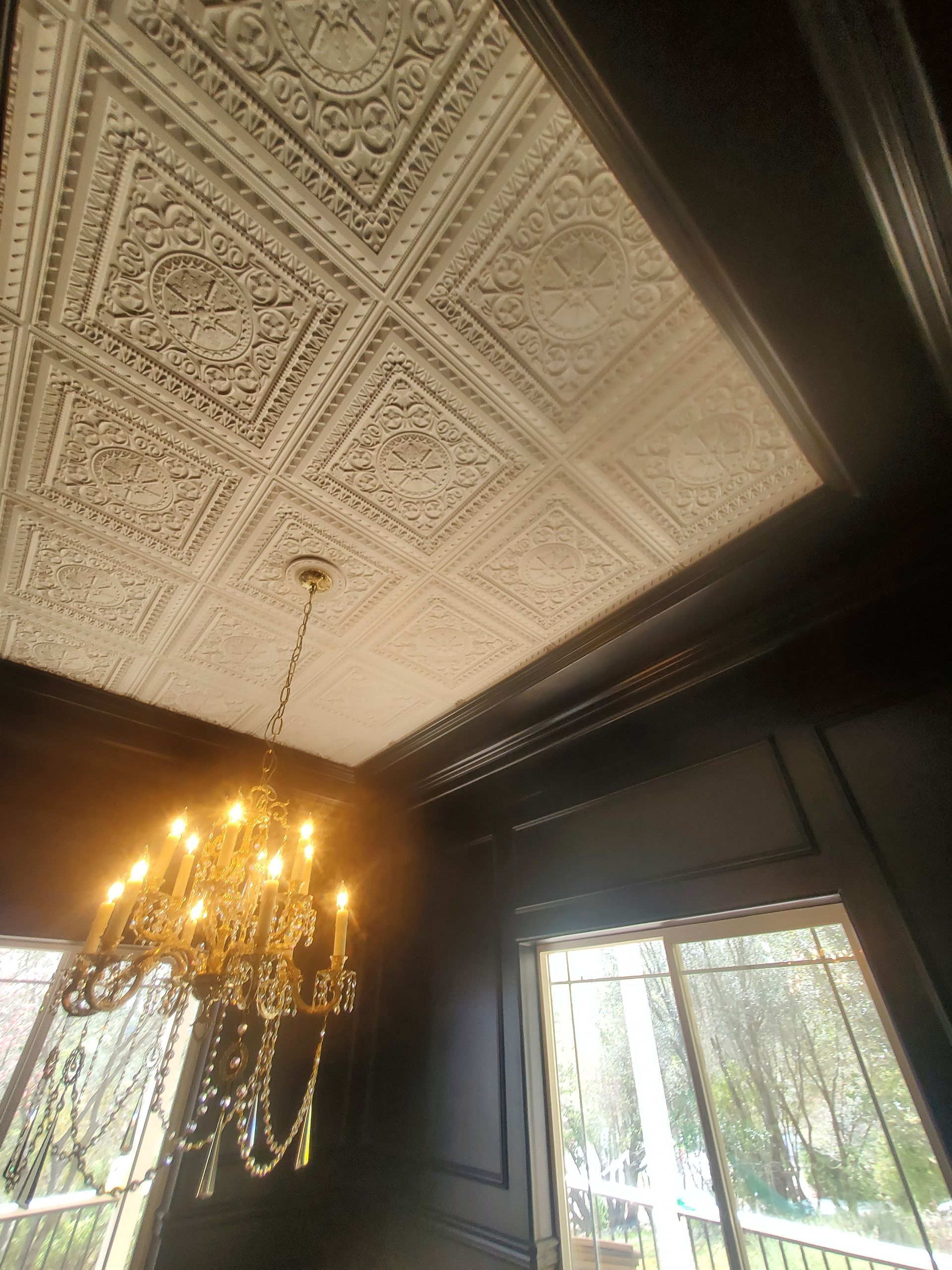 Ornate white ceiling with detailed patterns, black trim, and a chandelier.