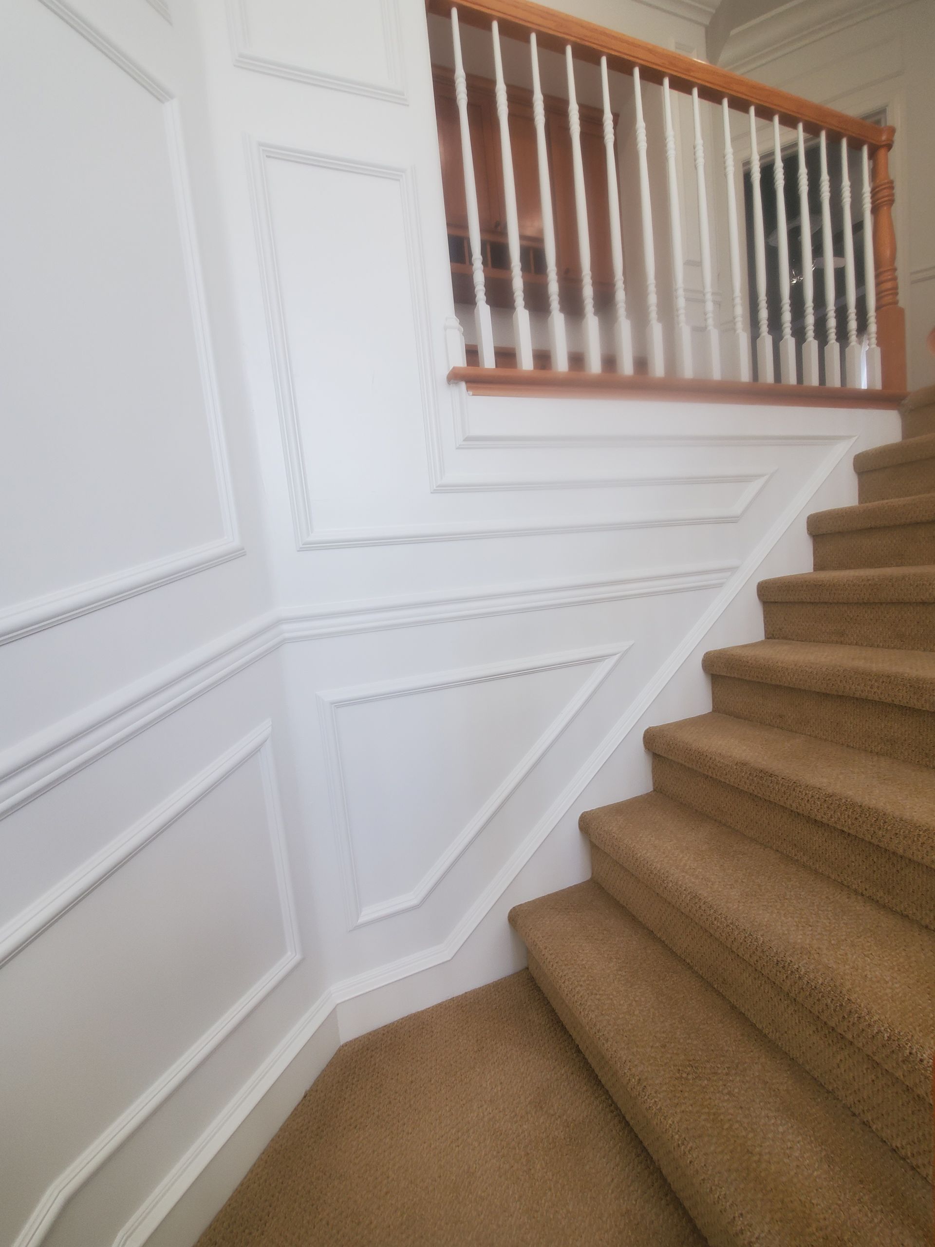 White paneled wall alongside a carpeted staircase with a wooden railing.