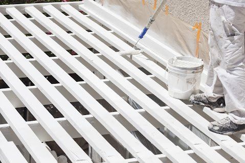 Person painting a white wooden deck with a roller, using white paint.