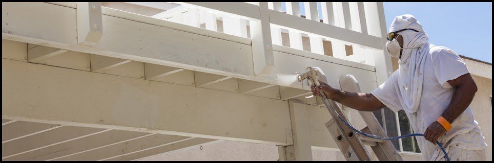 A painter spraying white paint onto a wooden structure while wearing protective gear.