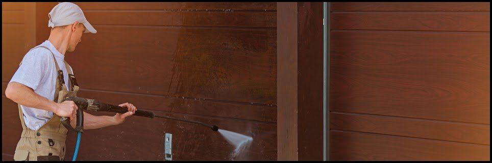 A person power washing a brown wooden fence, spraying water to clean it.