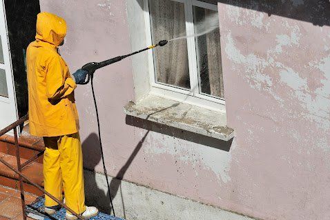 Person in yellow protective suit power washing a building's exterior.