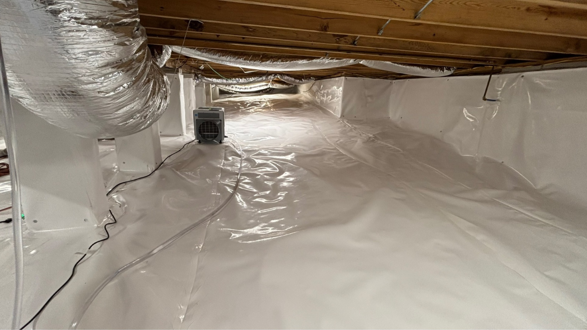 Insulated crawlspace with white vapor barrier, silver ducting, and wooden beams overhead