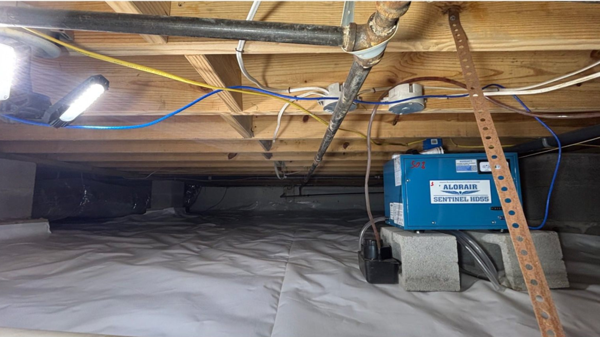 Blue HVAC unit in a crawl space with exposed wooden joists and ductwork under the floor