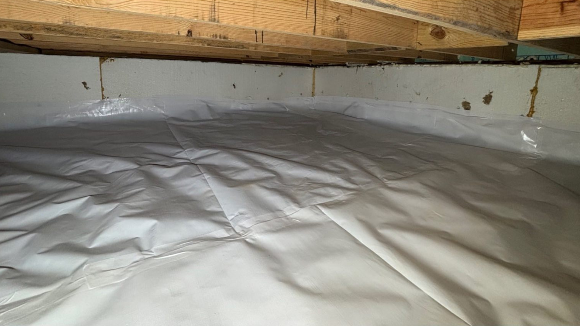 White insulated attic floor beneath wooden beams and a sloped roof.
