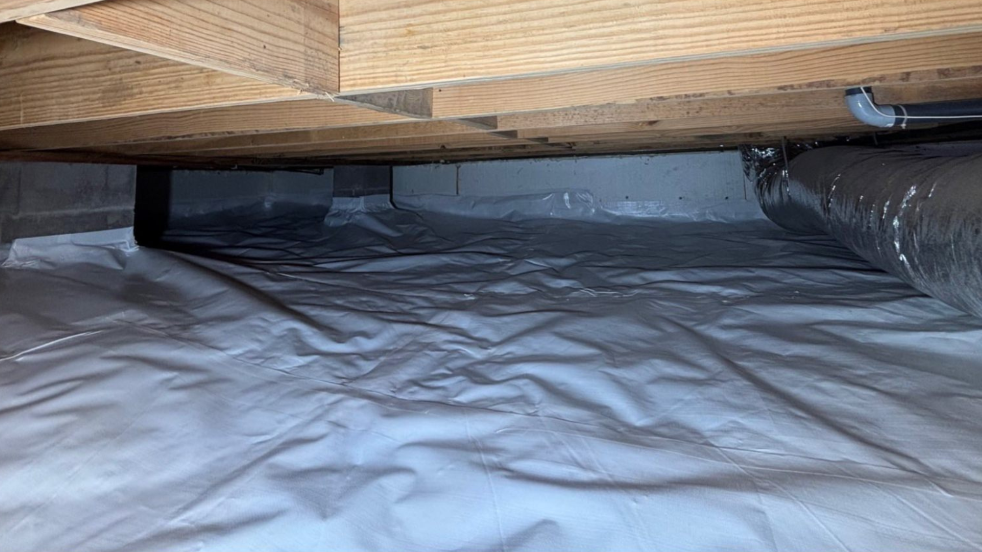 Under a wooden bed frame with a silver plastic tarp covering the floor and ductwork on the right