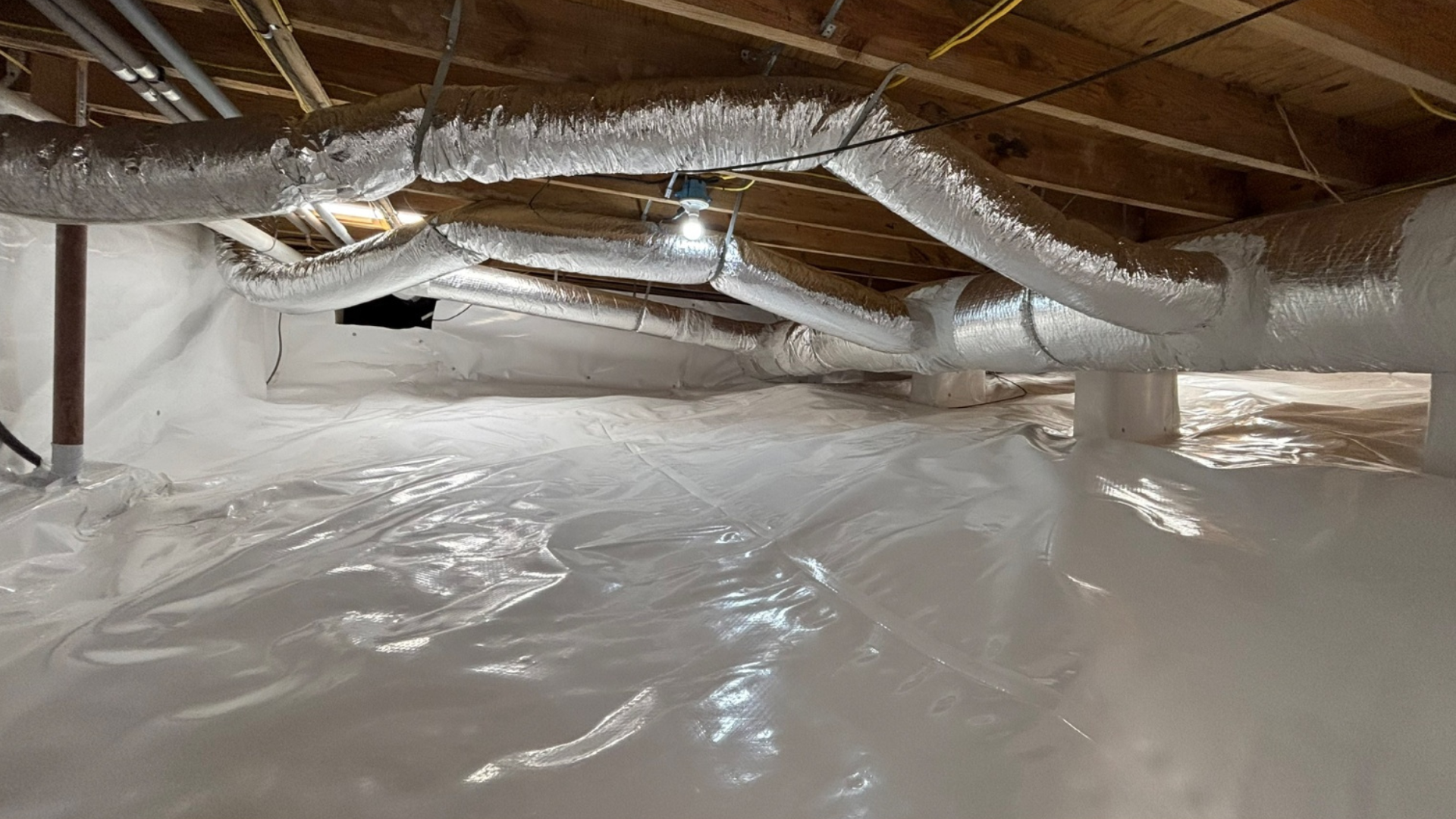 Crawlspace with exposed wooden beams, ductwork, and white plastic vapor barrier on the ground.