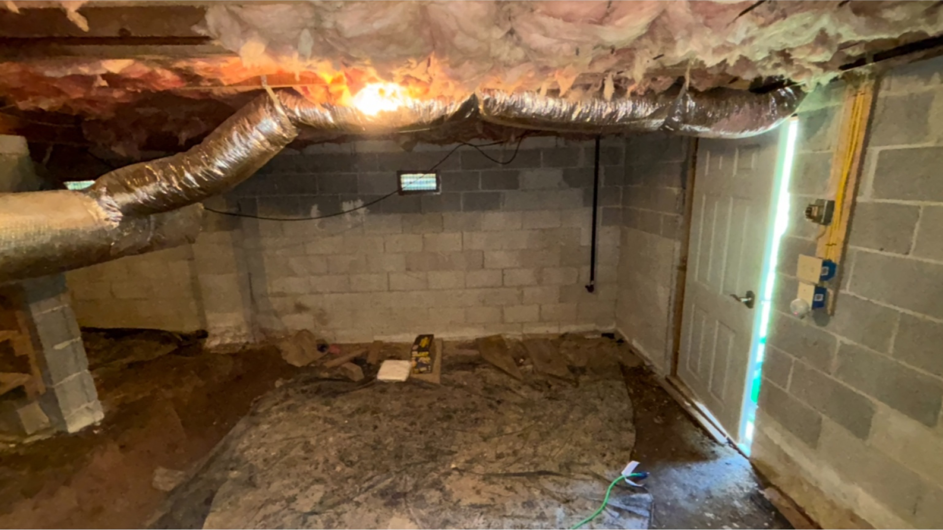 Unfinished basement crawlspace with concrete block walls, exposed insulation, ductwork, and dirt floor.