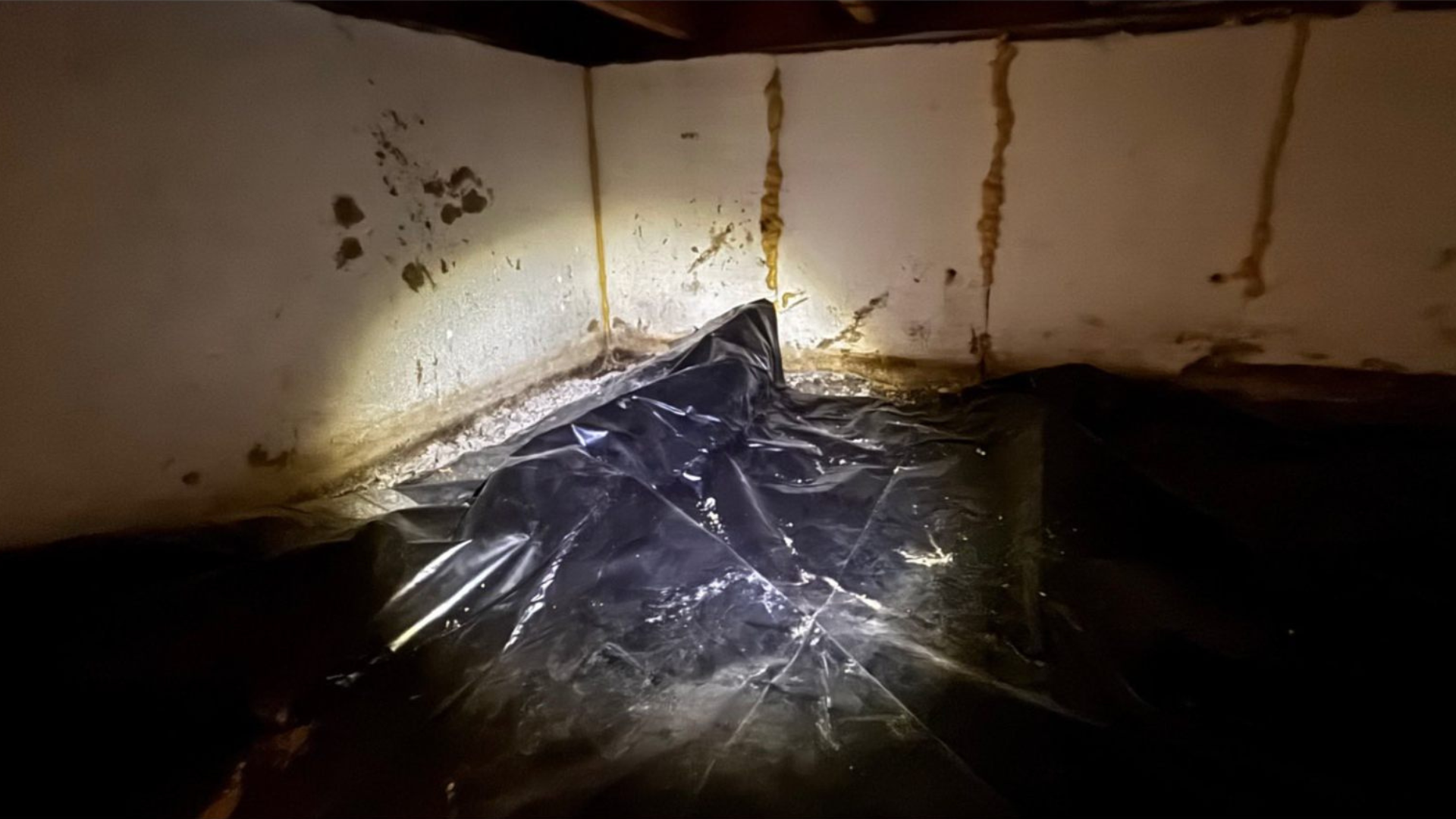 Dark plastic sheet covering a wet corner with rust stains and water pooling in a dim room