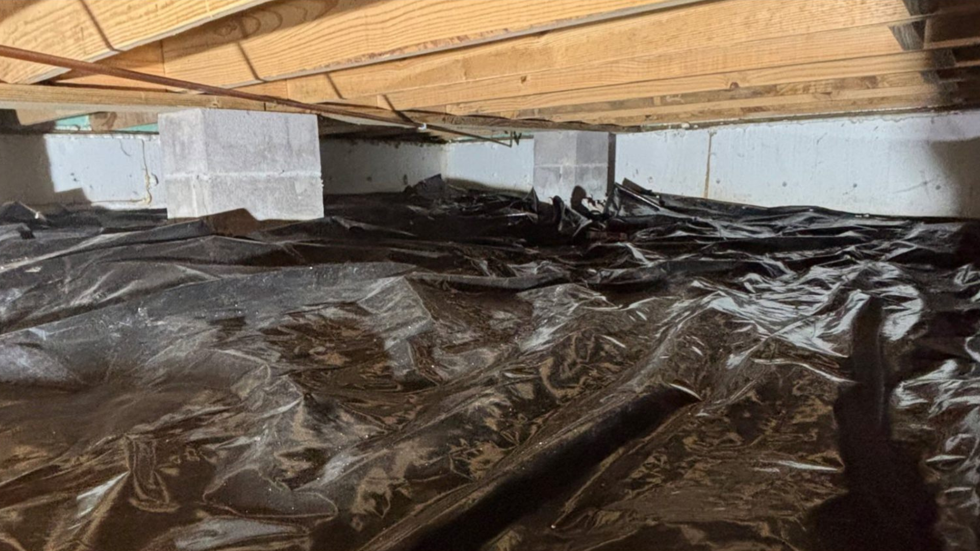 Crawl space under wooden floor with plastic vapor barrier and exposed insulation blocks