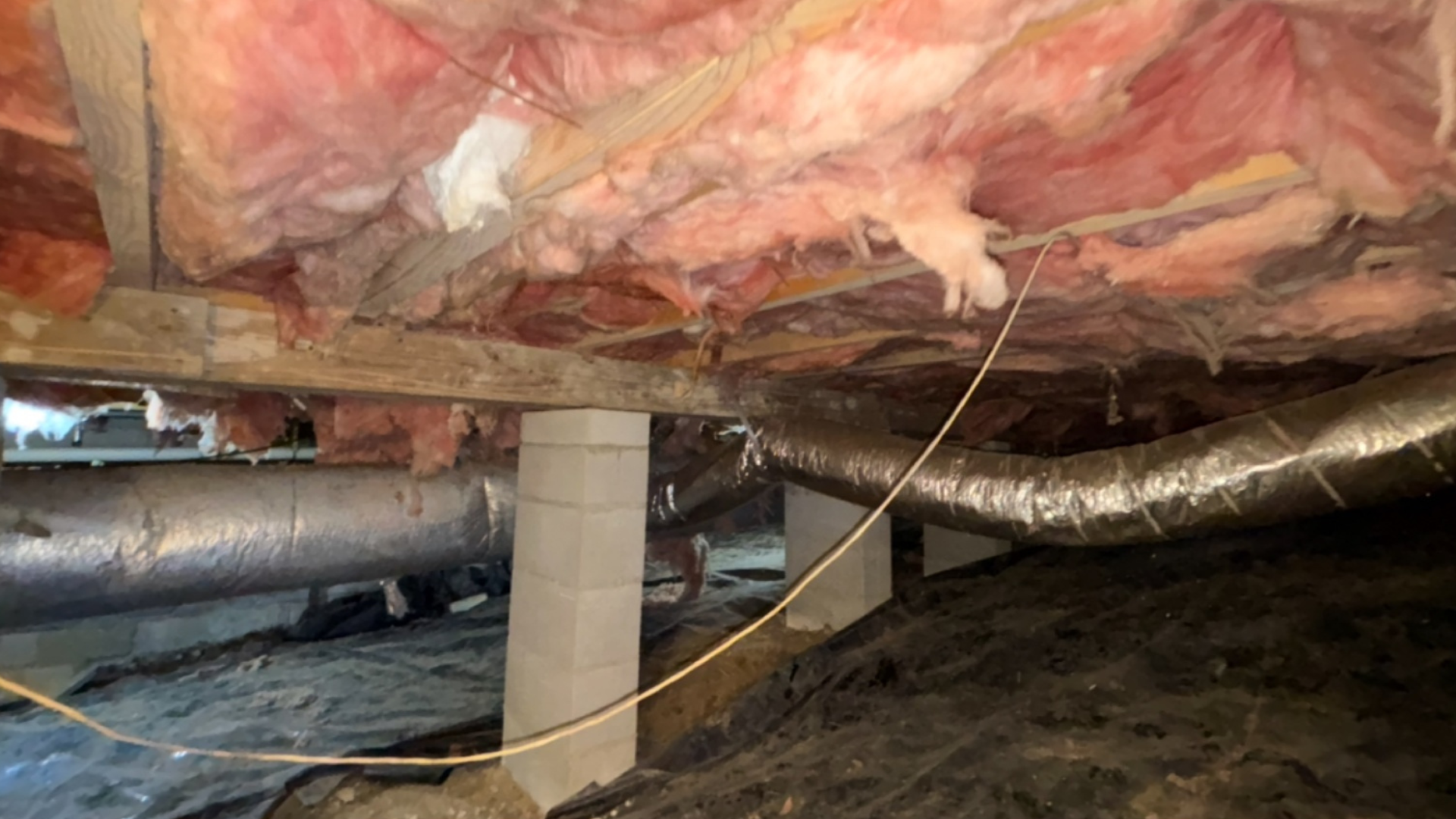 Insulated crawlspace with exposed ducts, pipes, and support columns under a house