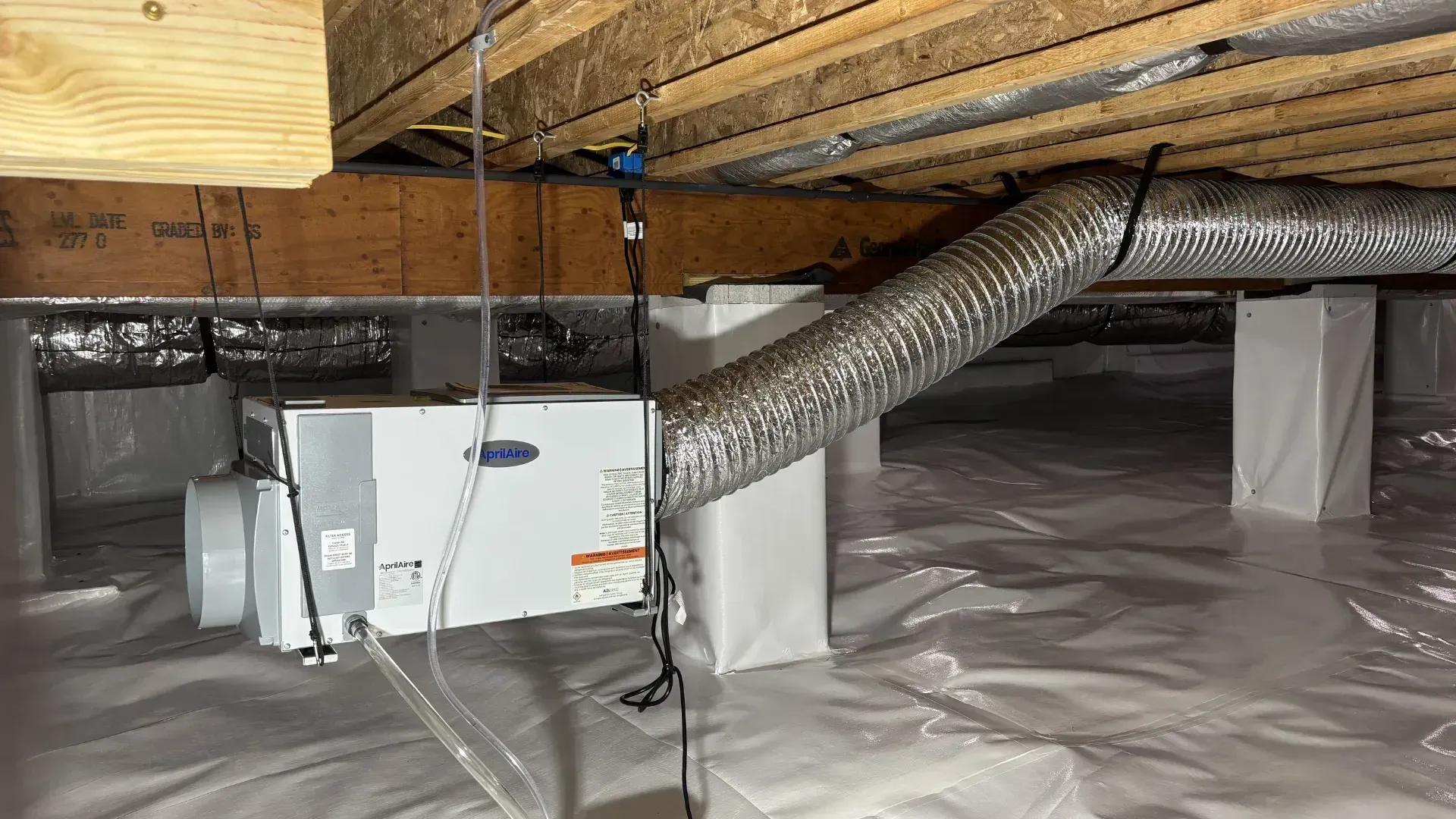 Crawlspace with insulated ducts, white vapor barrier on the floor, and exposed wooden joists overhead