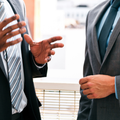 Two businesspeople in suits gesturing during a discussion indoors