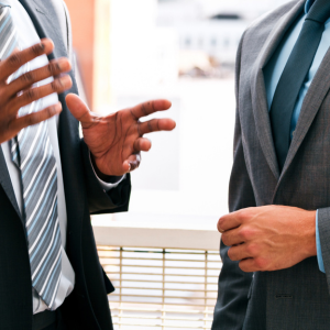 Two businesspeople in suits gesturing during a discussion indoors