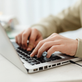 Hands typing on a laptop keyboard at a desk, with a white background.