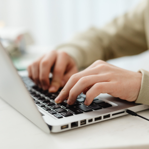 Hands typing on a laptop keyboard at a desk, with a white background.