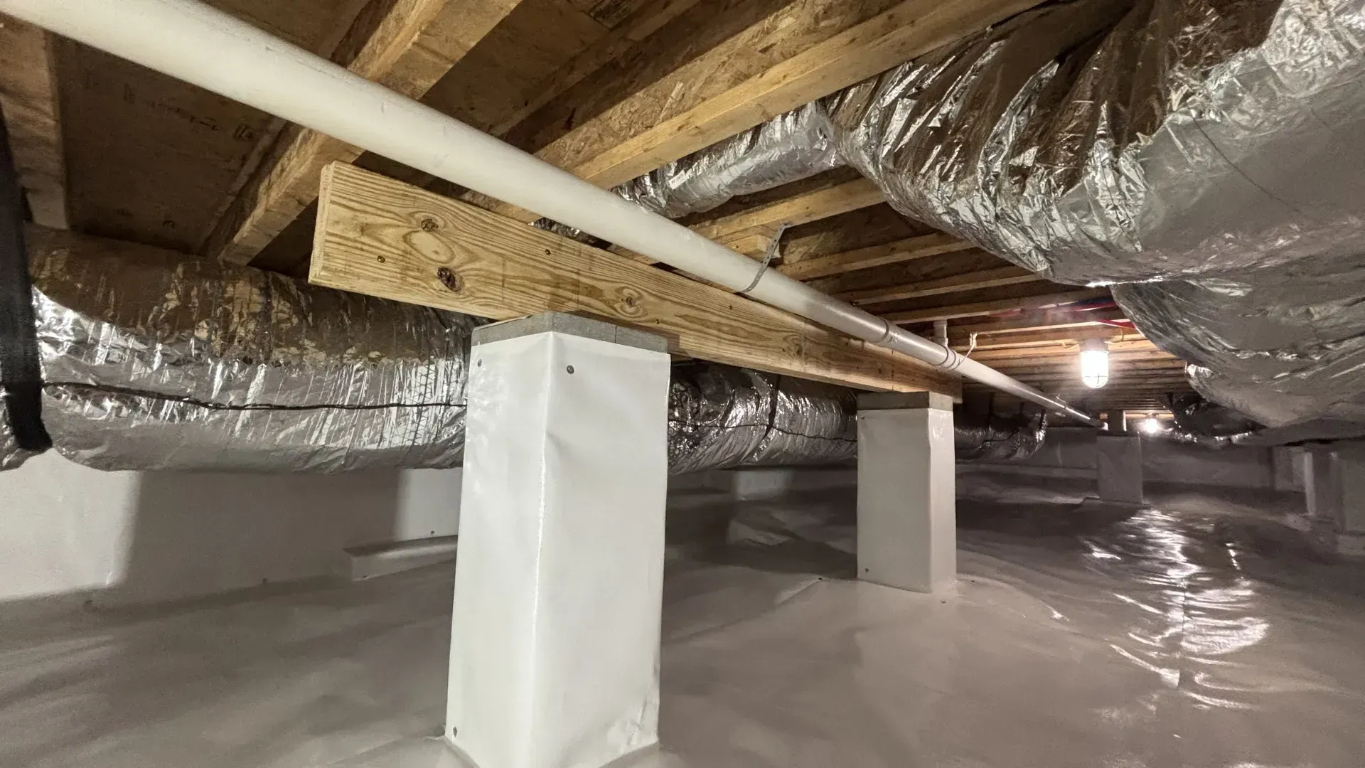 Crawlspace with exposed beams, insulated ducts, and plastic-covered floor under a house