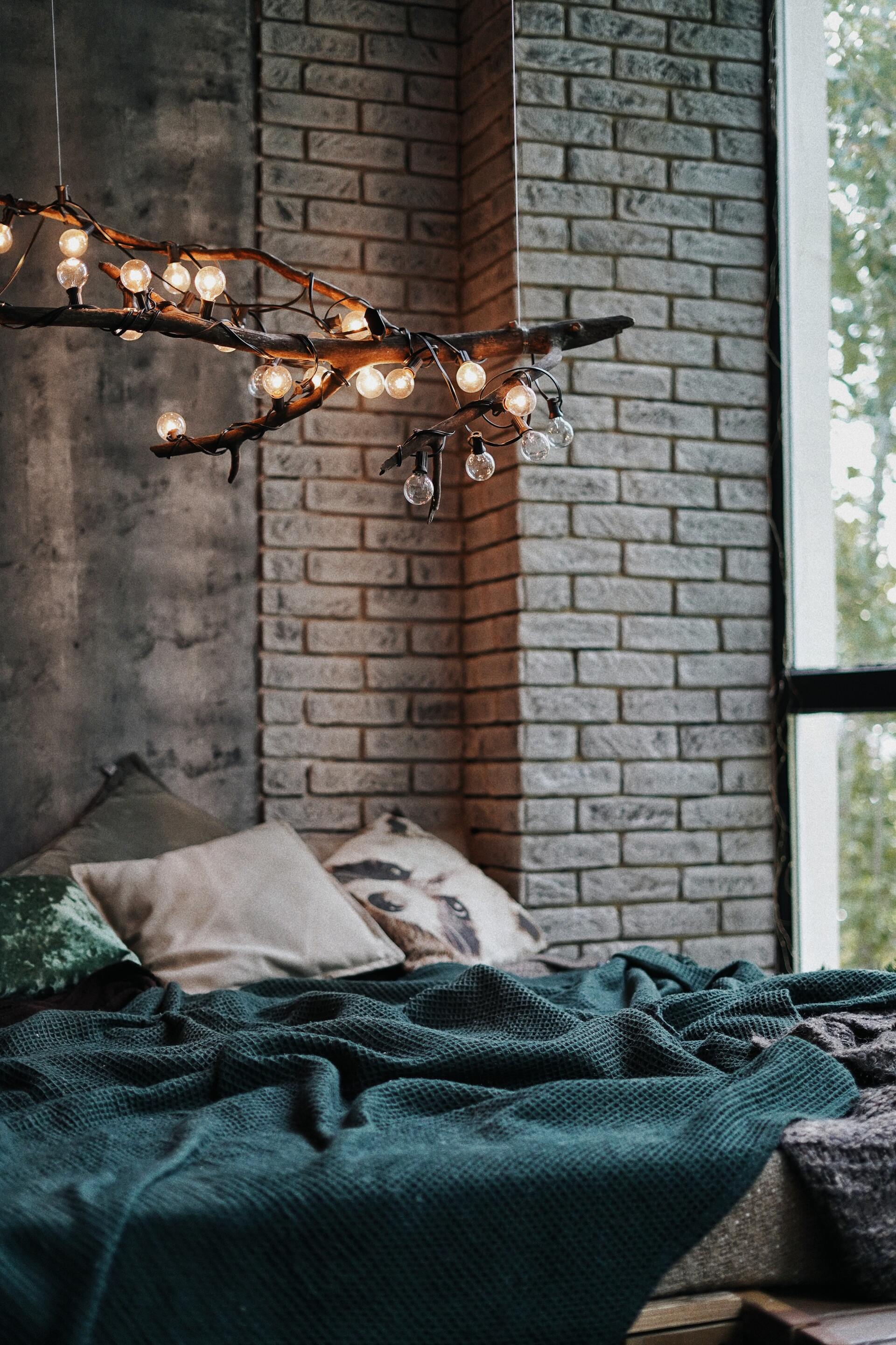 Cozy bedroom with a bed by a brick wall, lit by warm string lights beside a window