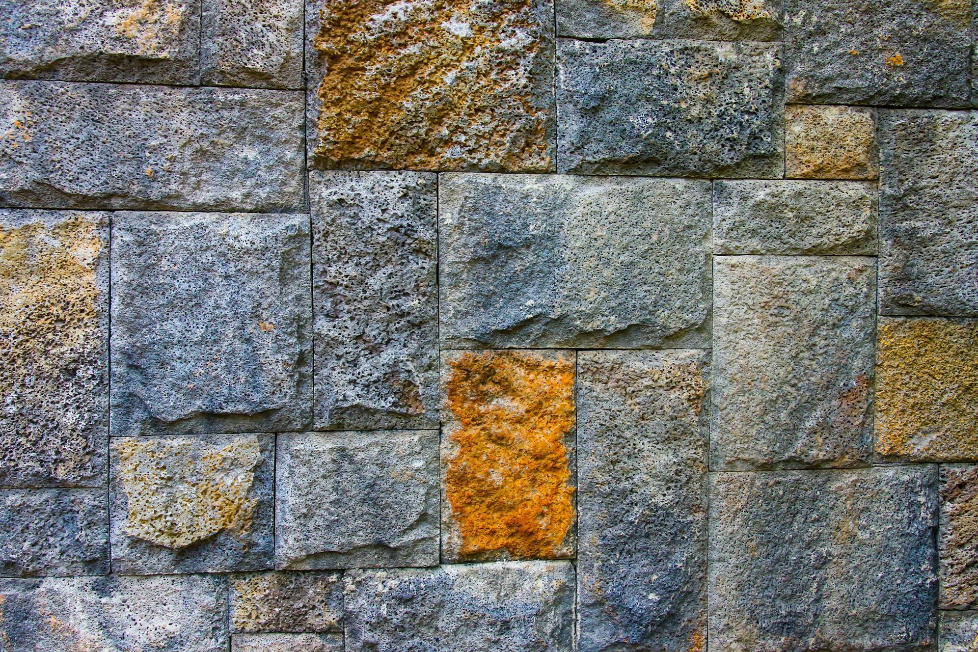 Stone wall made of gray and tan blocks with a few orange-stained stones