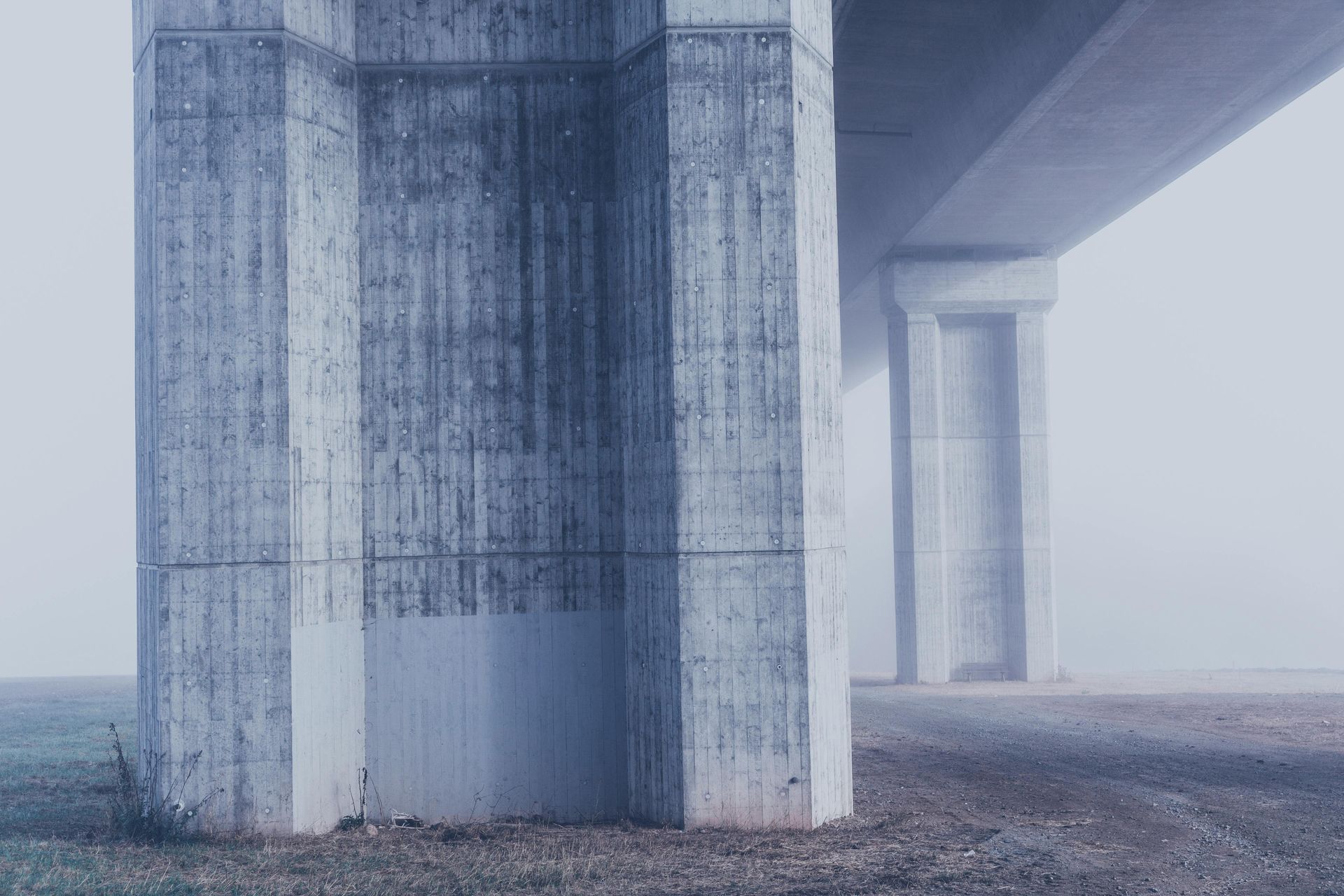 Foggy concrete bridge pillars over a gravel landscape