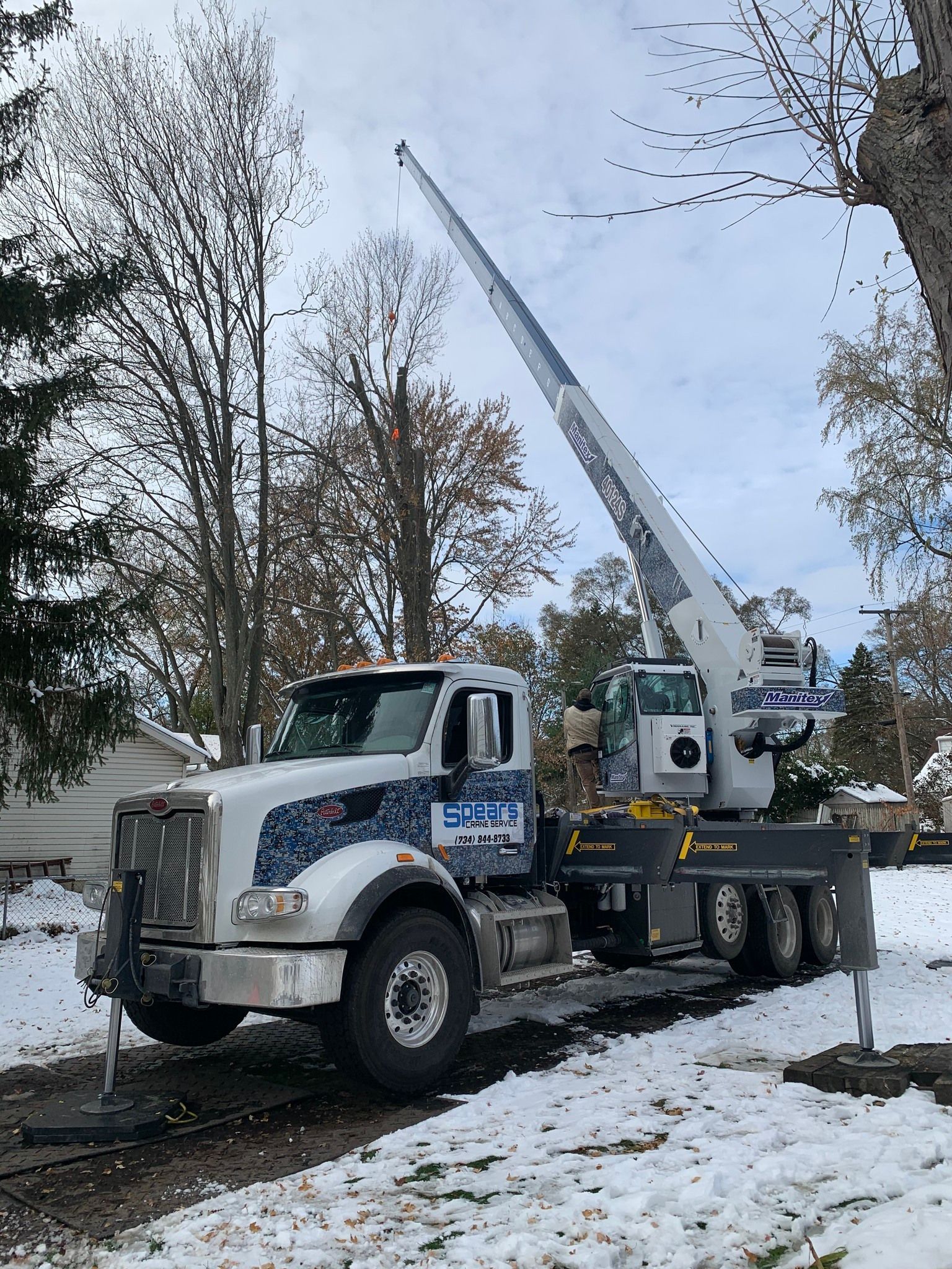White tree-trimming truck with extended boom in snowy yard.