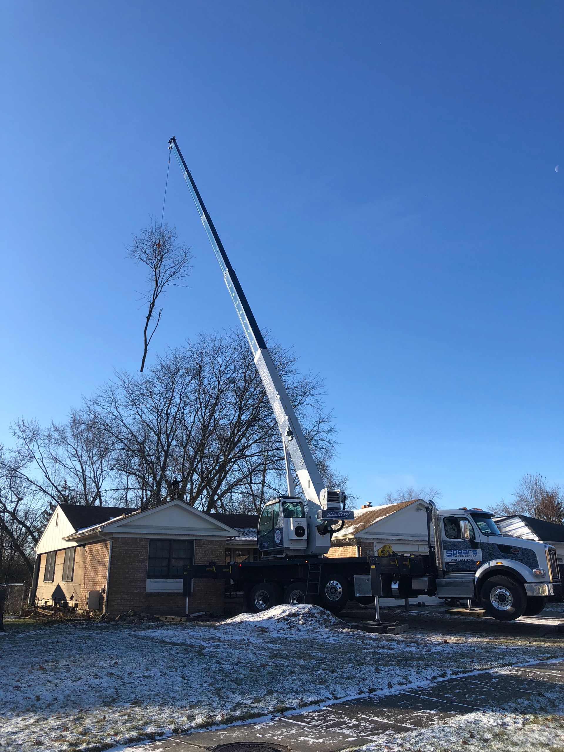 Crane lifting debris near a small house on a sunny day.