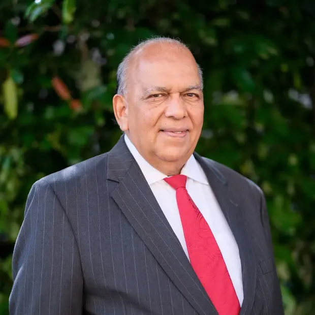 A man in a suit and tie is standing in front of a tree.