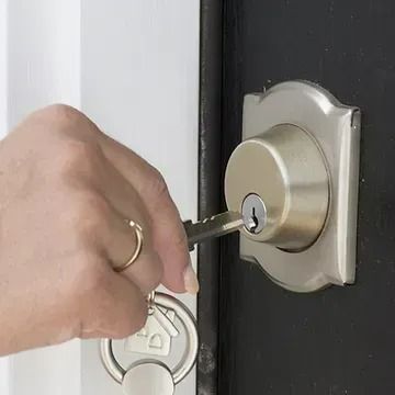 A person’s hand inserting a metal key into a brass-colored deadbolt lock on a dark door.