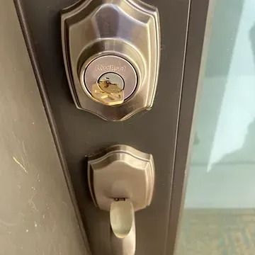 A brass key inserted into the deadbolt lock of a brushed nickel door handle on a dark brown door.