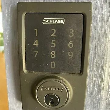 A dark gray Schlage electronic keypad door lock with a physical key cylinder, mounted on a light gray door frame.