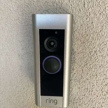 A silver Ring video doorbell mounted on a textured, light-colored wall.