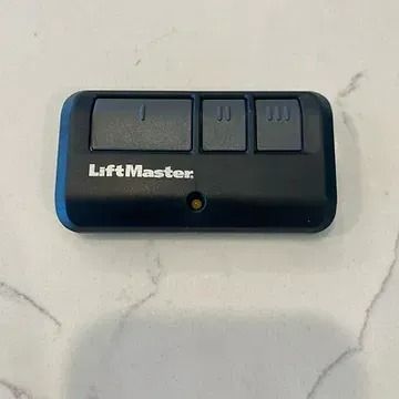 A black, rectangular LiftMaster garage door remote with three buttons, resting on a white, gray-veined countertop.