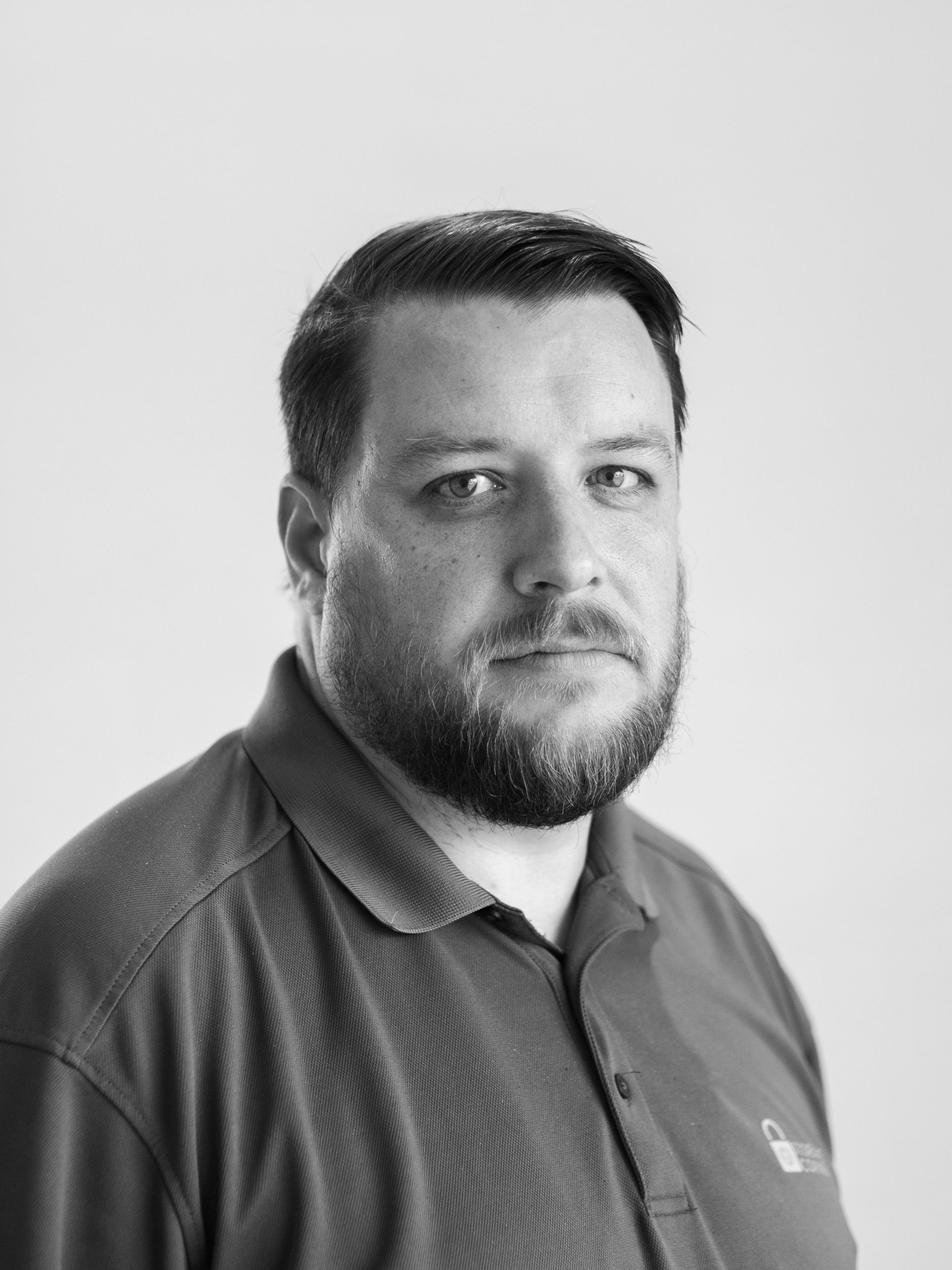 A black and white photo of a man with a beard wearing a polo shirt.