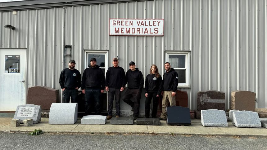 People standing outside Green Valley Memorials beside rows of gravestones and monuments.