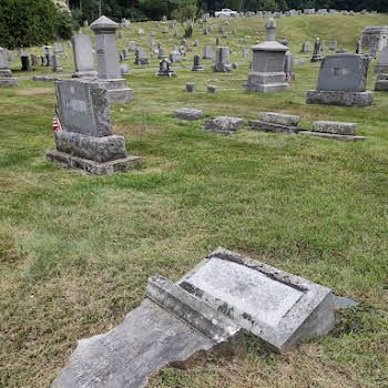 Damaged gravestone lying in front of a cemetery with several upright headstones in the background
