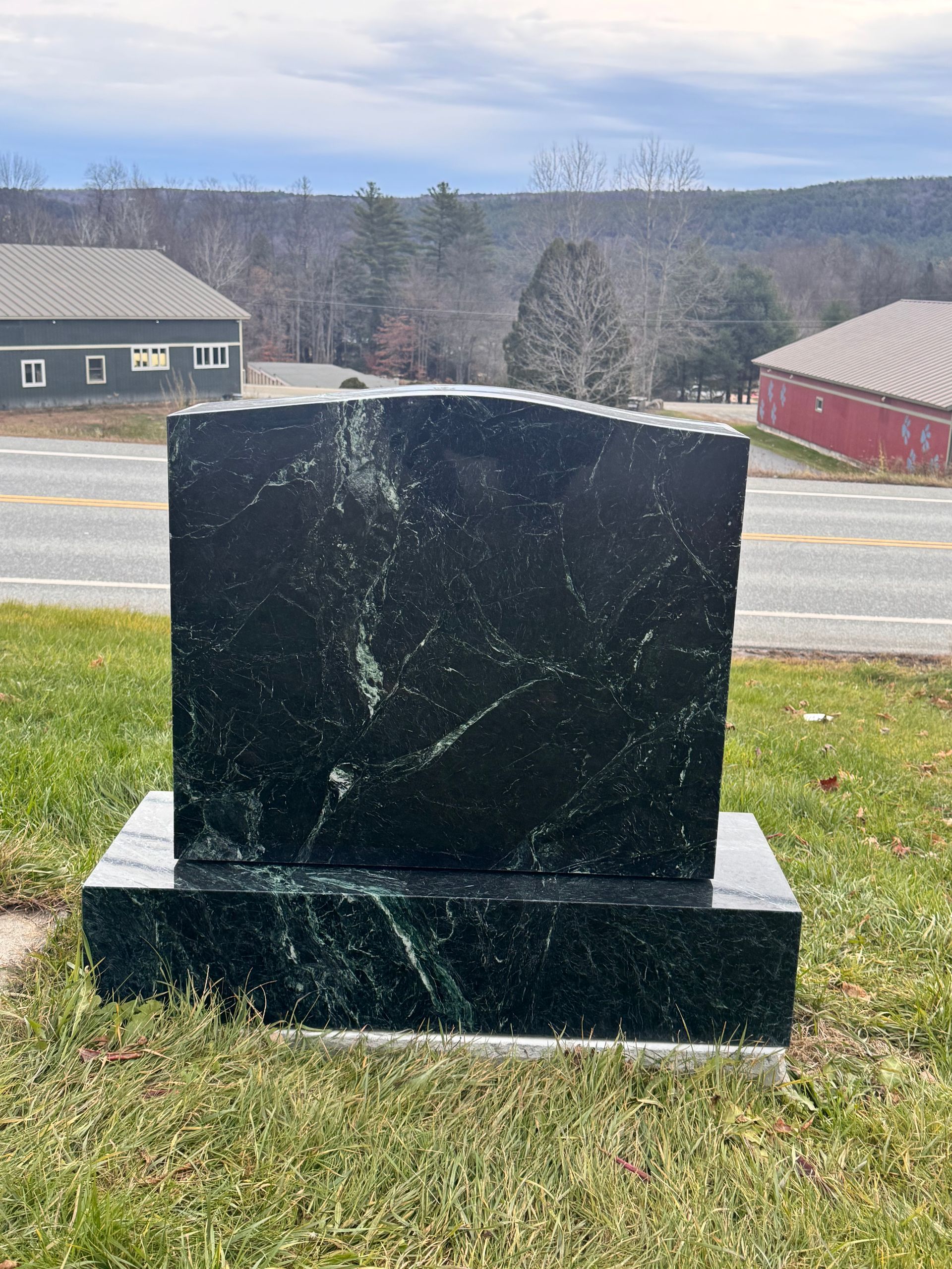 Black granite monument on a grassy roadside with buildings and hills in the background