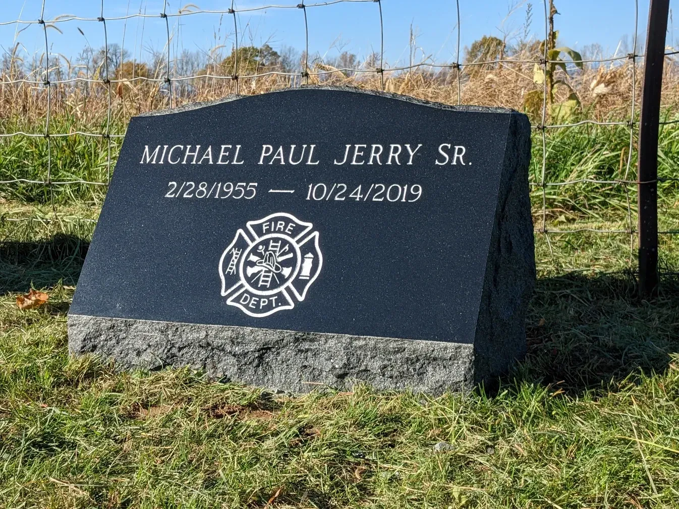 Black firefighter memorial headstone with “Michael Paul Jerry Sr.” and dates, in a grassy cemetery.