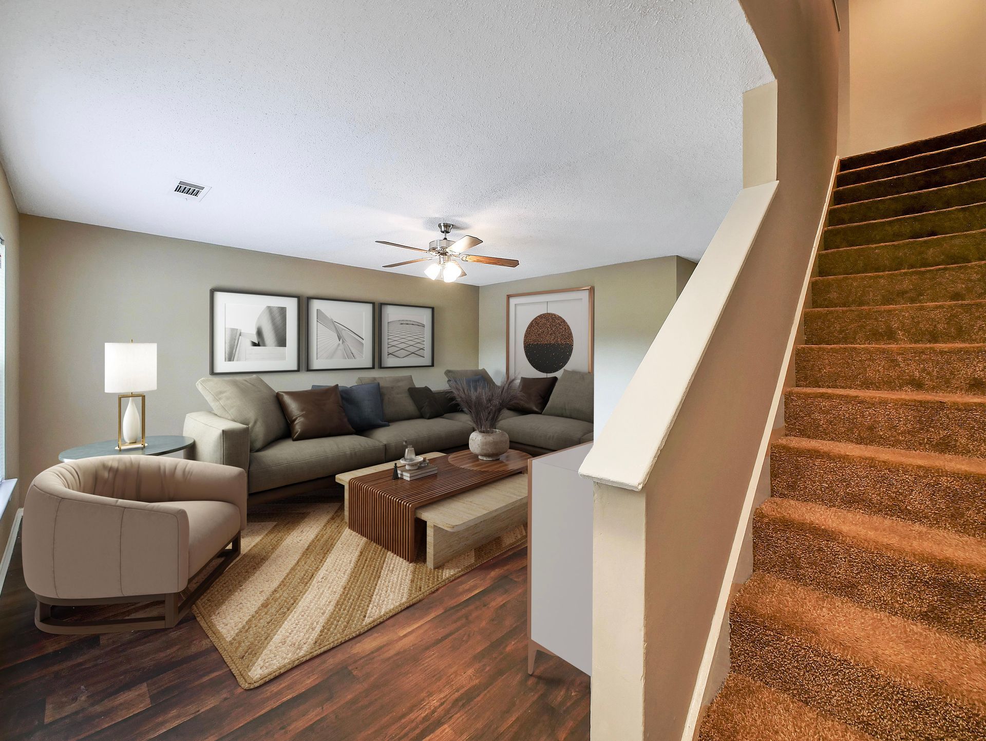 A cozy living room with a gray sectional, light armchair, wood coffee table, and patterned rug, near a carpeted staircase.