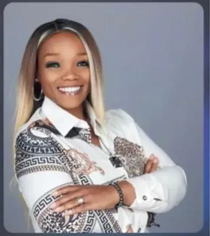 Smiling person with crossed arms wearing a patterned shirt against a gray background