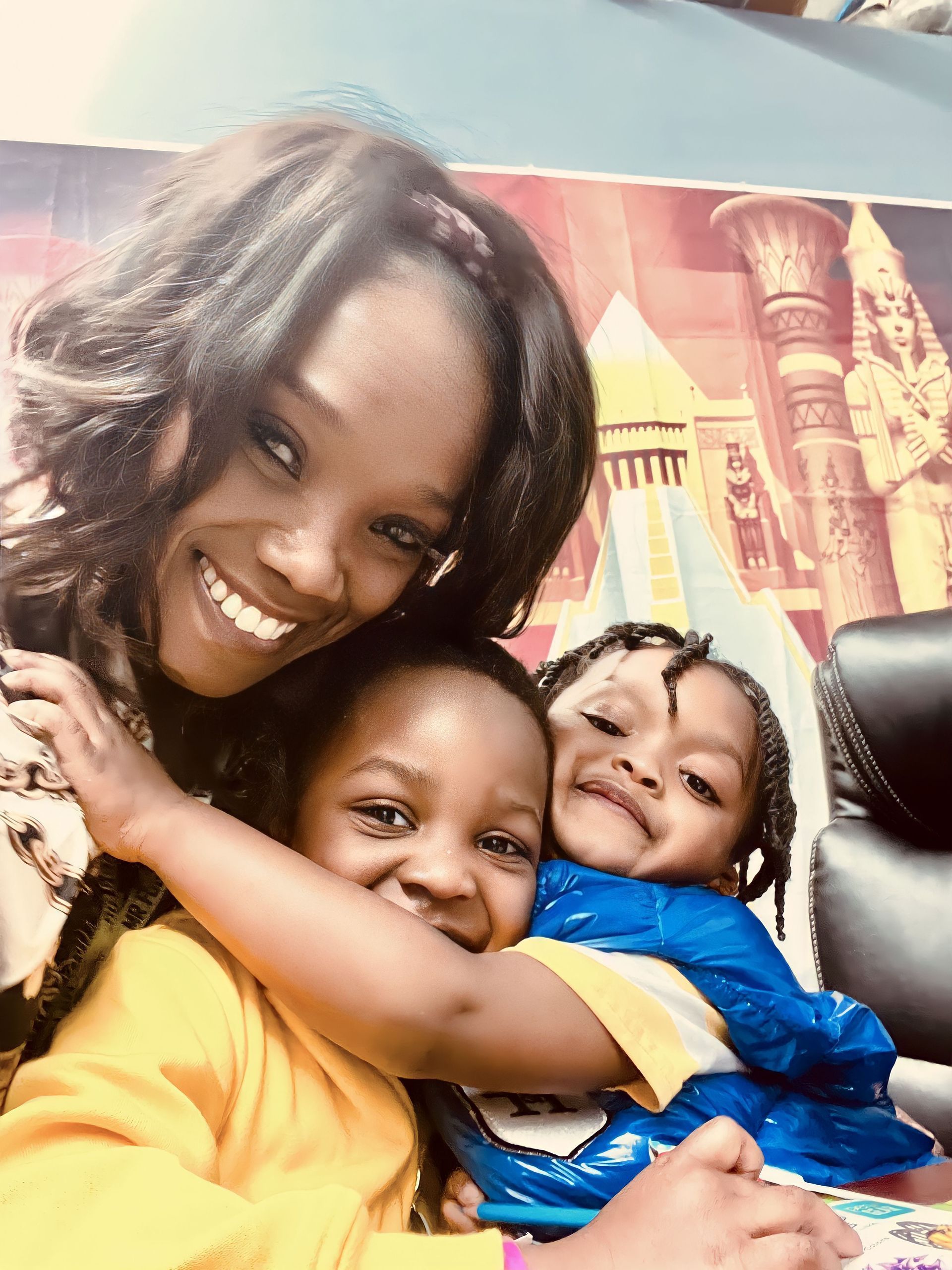 Three smiling people hugging in front of a colorful mural