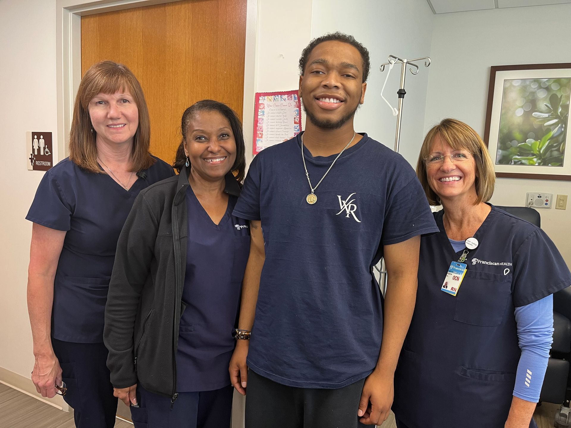 Four people smiling in navy shirts standing together in a hallway or office.