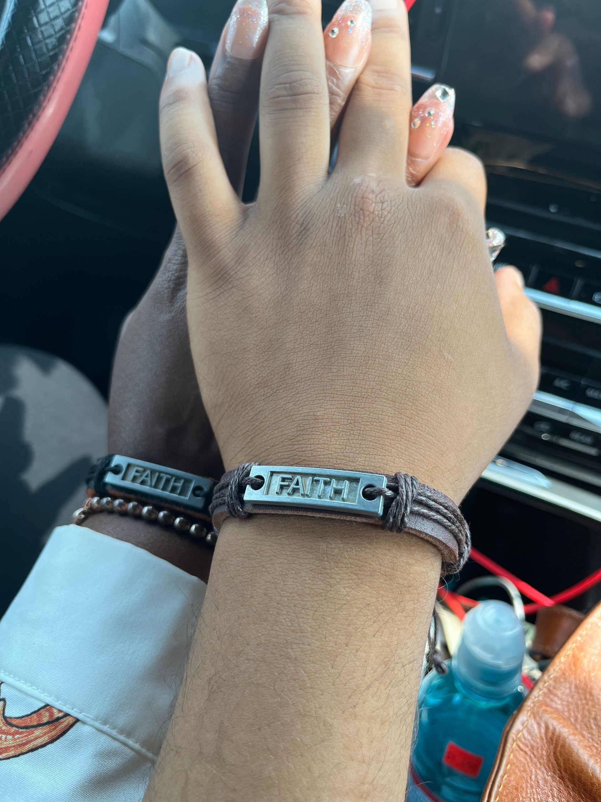 Hand with bracelets resting on a car dashboard, holding hands with another person.