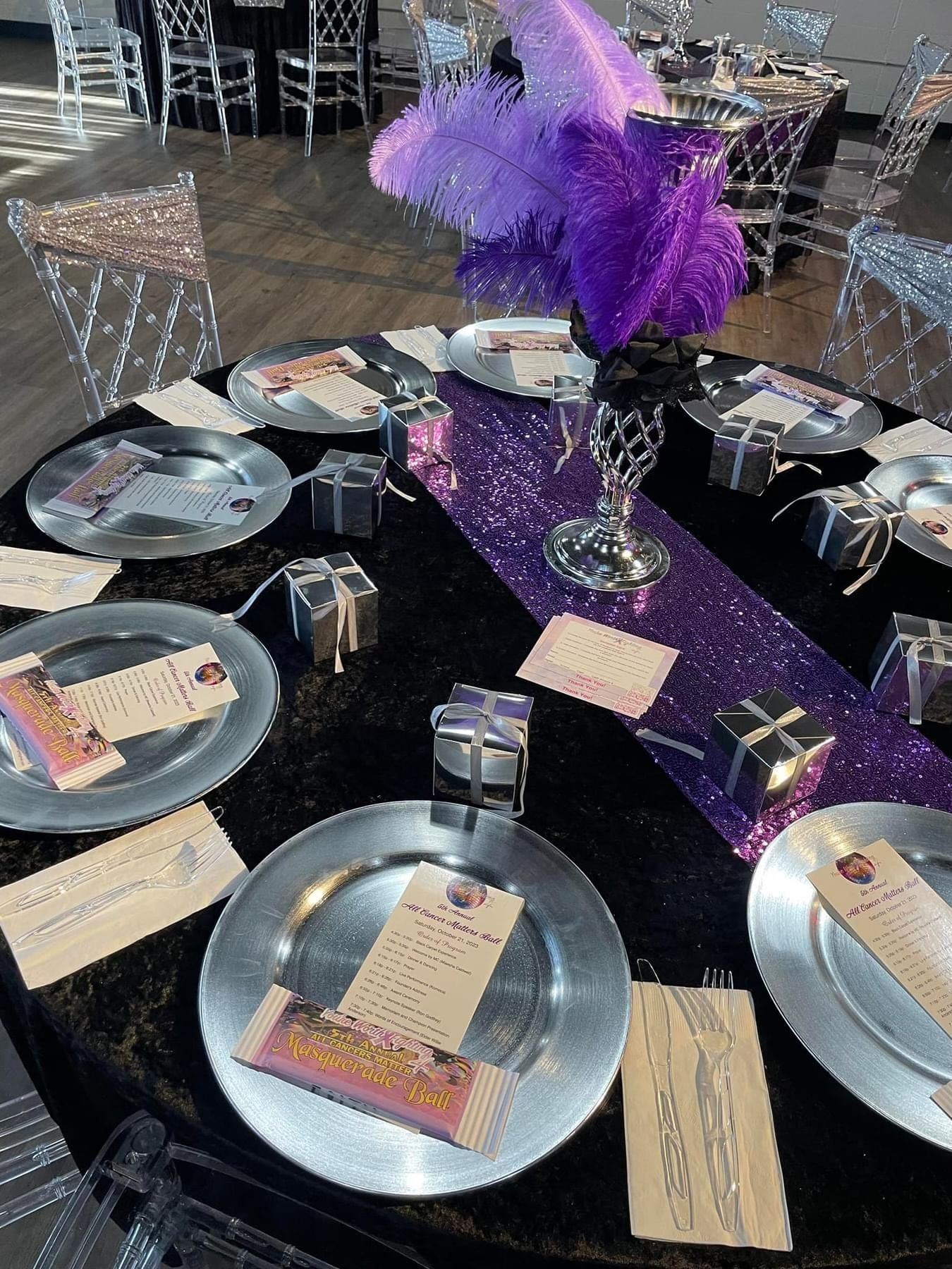 Purple feather centerpiece on a decorated banquet table with silver plates and place cards.